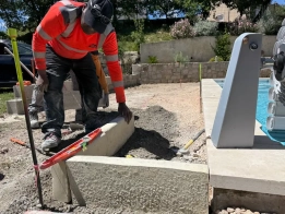 préparation de la terrasse avant l’application de moquette de pierre à gréasque Travailleur construit un mur près d'une piscine.