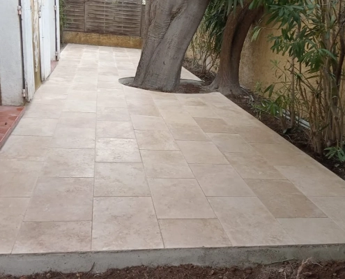 Terrasse en travertin achevée le long d'une maison à Marseille, avec découpes du dallage autour des arbres